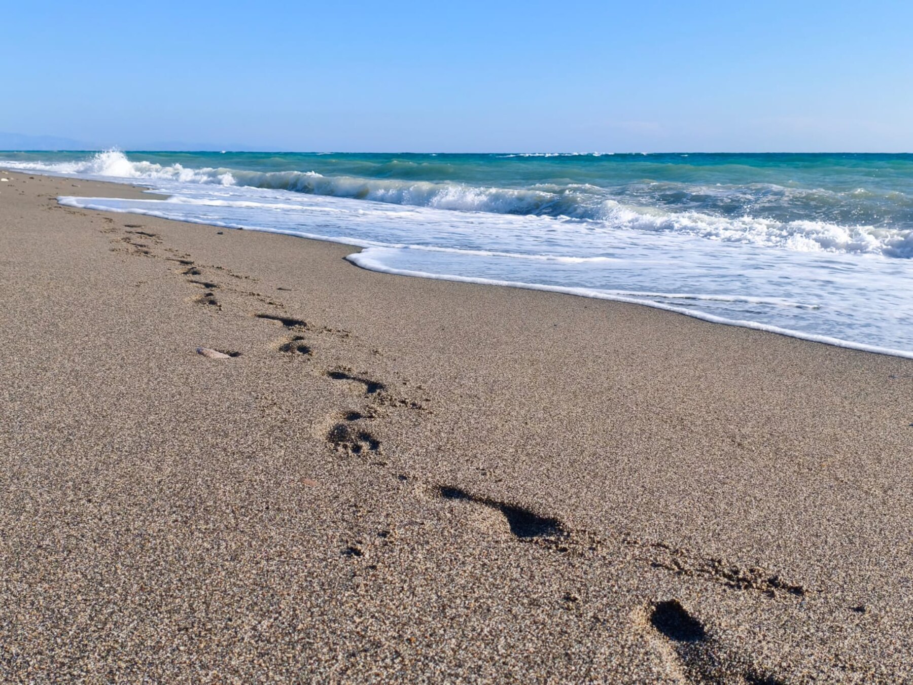 Footsteps in sand beside ocean waves